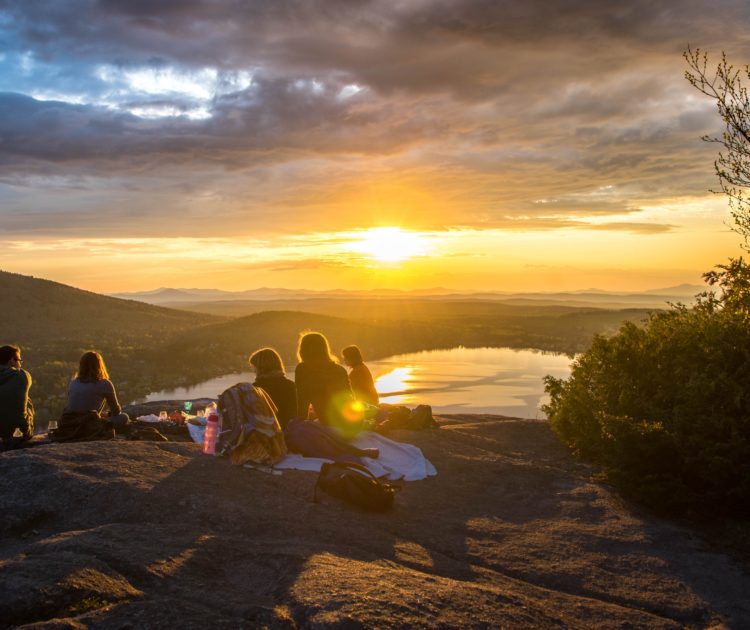 Group sitting together on mountain top at sunset