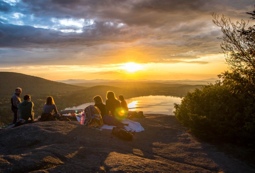 Group sitting together on mountain top at sunset