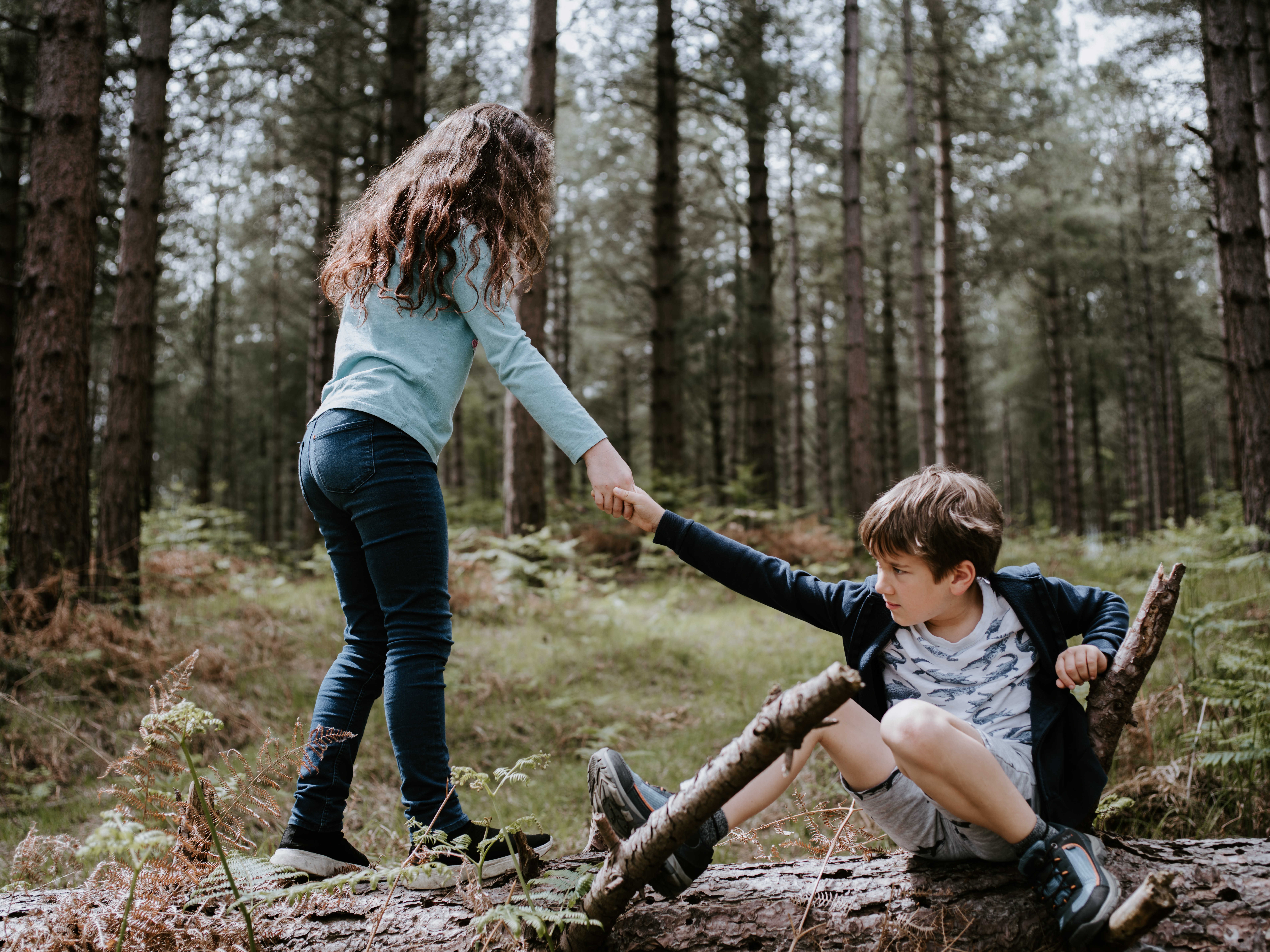 Girl helping boy stand up in the forest