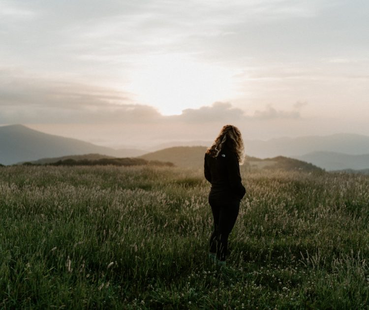 Woman walking through field at sunrise