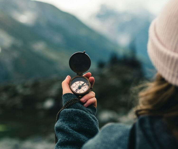 Woman standing on a mountain, holding a compass and looking toward the horizon. The image symbolizes guidance and direction, aligning with the theme "How to find the right therapist."