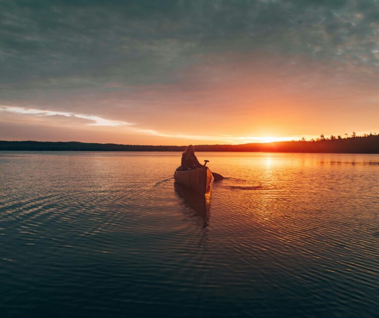 Woman paddling a canoe on a calm lake at sunset, reflecting peaceful surroundings. The serene moment evokes a sense of balance and well-being, aligning with the theme "what is behavioral health?"