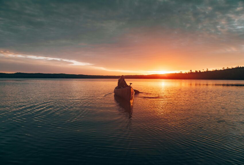 Woman paddling a canoe on a calm lake at sunset, reflecting peaceful surroundings. The serene moment evokes a sense of balance and well-being, aligning with the theme "what is behavioral health?"