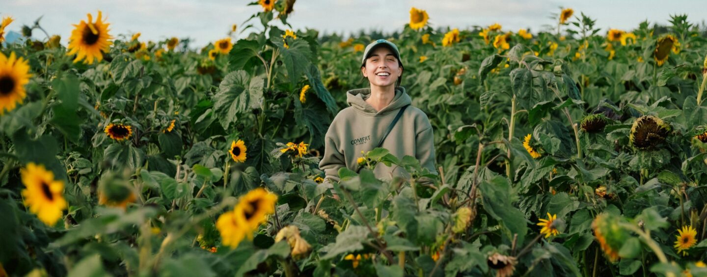 A woman stands in a field of sunflowers, symbolizing the healing and recovery provided by 24/7 mental health and addiction services.