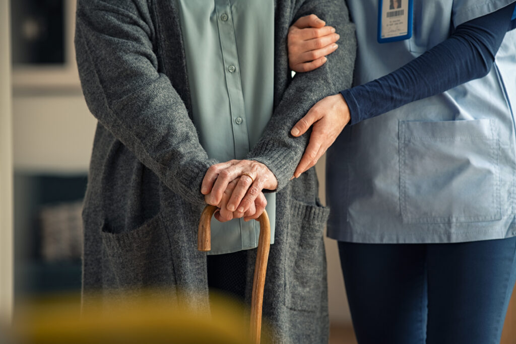 A nurse helps a geriatric patient walk with a cane.