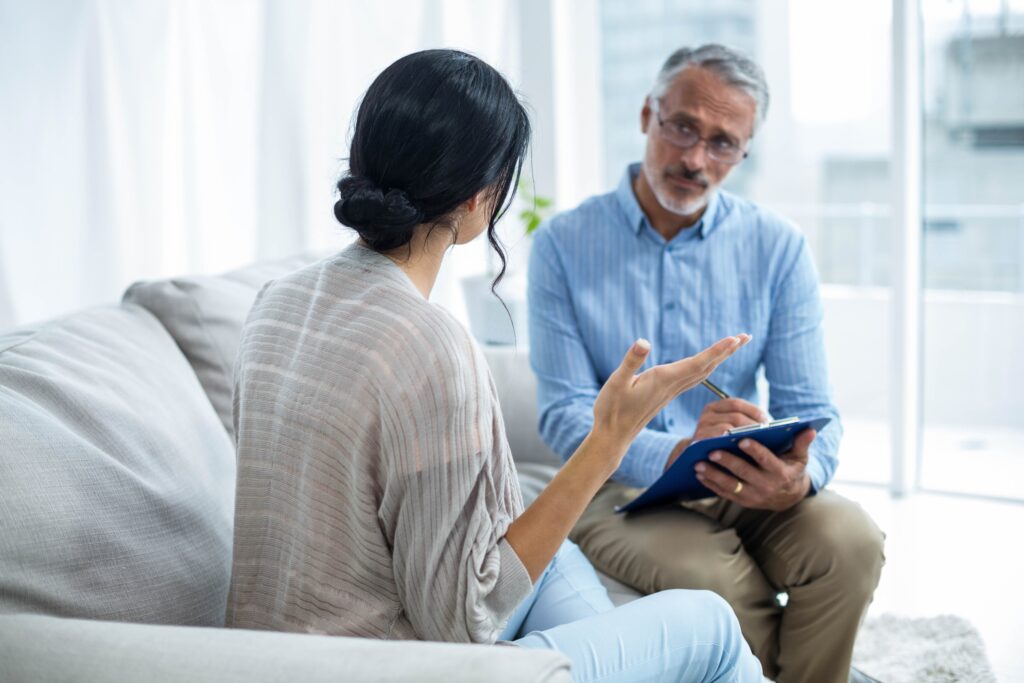 A therapist listens to a patient speak. The term "therapist" could refer to a psychologist or to dedicated professional such as a Licensed Mental Health Counselor (LMHC), Licensed Clinical Social Worker (LCSW) or Licensed Master Social Worker (LMSW).