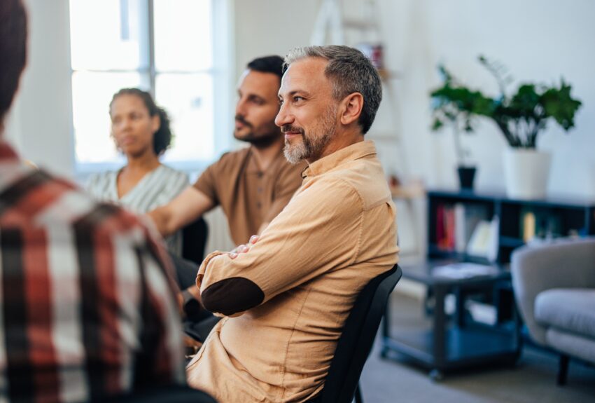 A focused mature man follows the flow of the story, sitting and listening to the others during group therapy for Obsessive-Compulsive Disorder.