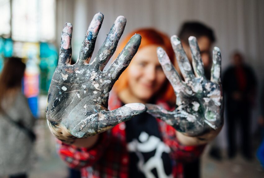 Young person showing hands covered with paint during mass art therapy session.