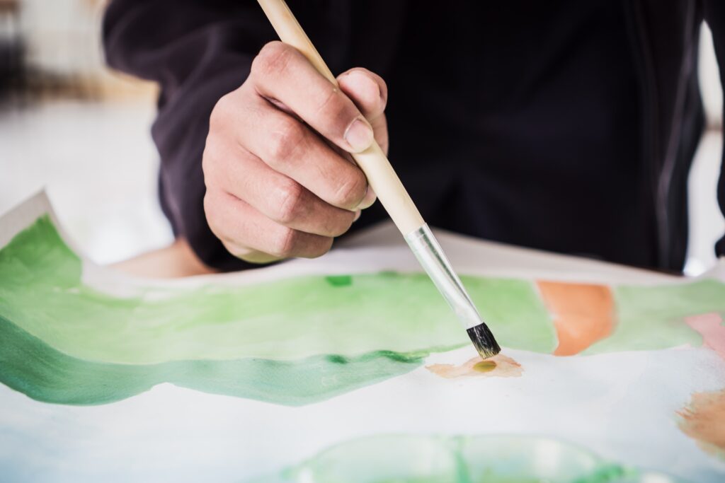 A patient painting watercolor abstract of landscape with brush as part of art therapy.