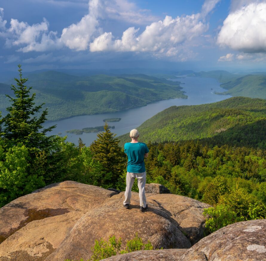 A man stands on a high peak overlooking a lake in Upstate New York.