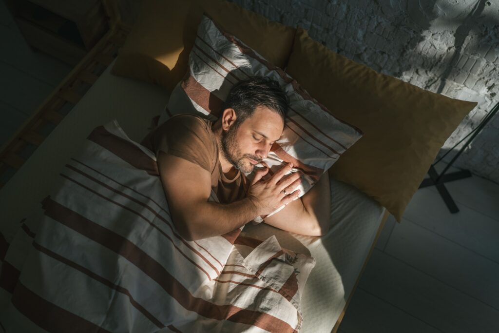 Man sleeping on his side in a cozy bed as morning sunlight warms his face.