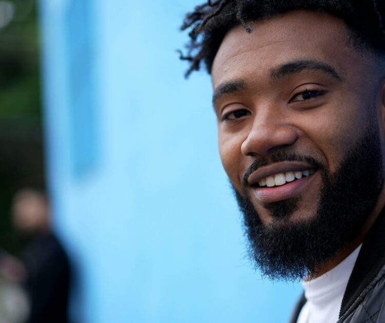 A man smiles in front of a bright blue wall.