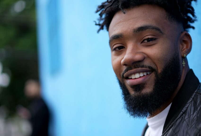 A man smiles in front of a bright blue wall.