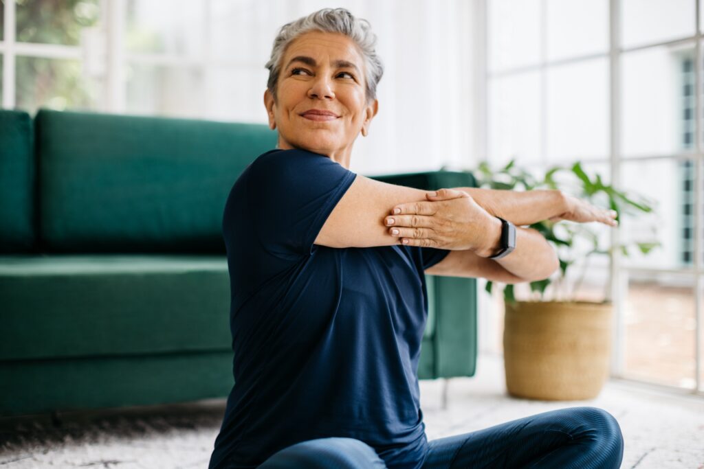 Happy and healthy senior woman doing a shoulder mobility exercise at home, working out with a cross arm stretch in her yoga session.